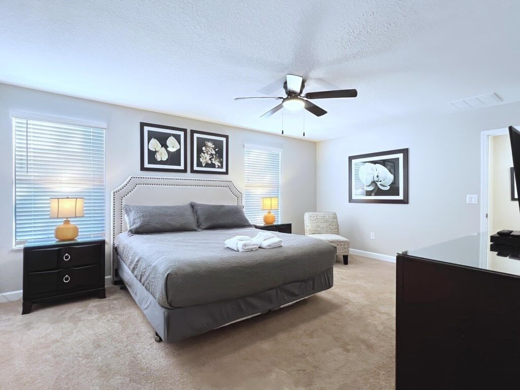 Un dormitorio con cama, mesitas de noche, una silla y un ventilador de techo.
