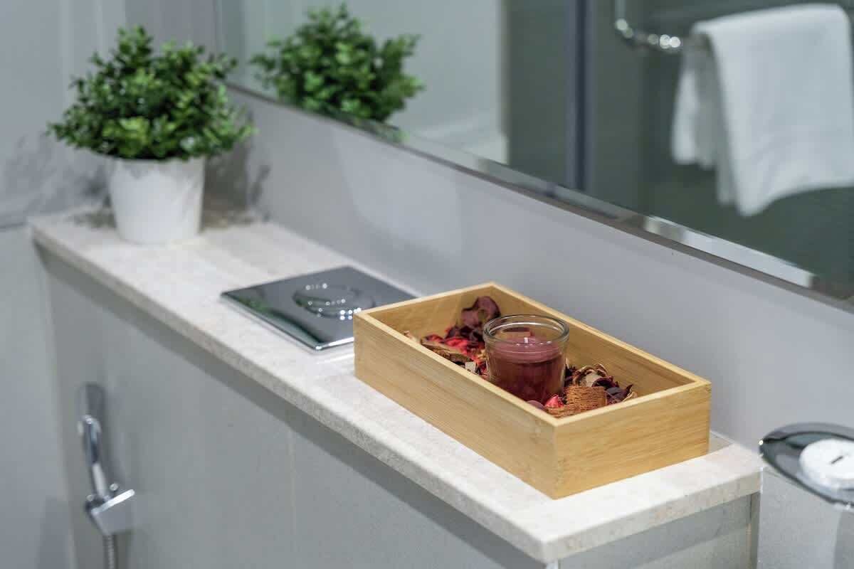Een badkamer met een houten doos, waarin een glas en gedroogde bloemen op een aanrecht staan.