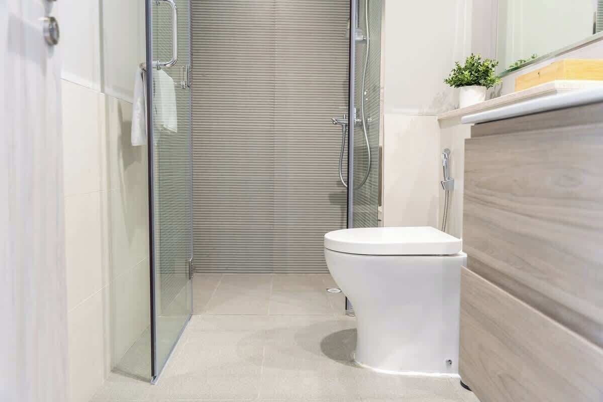 Un baño moderno con cabina de ducha de vidrio, inodoro blanco y tocador de madera.