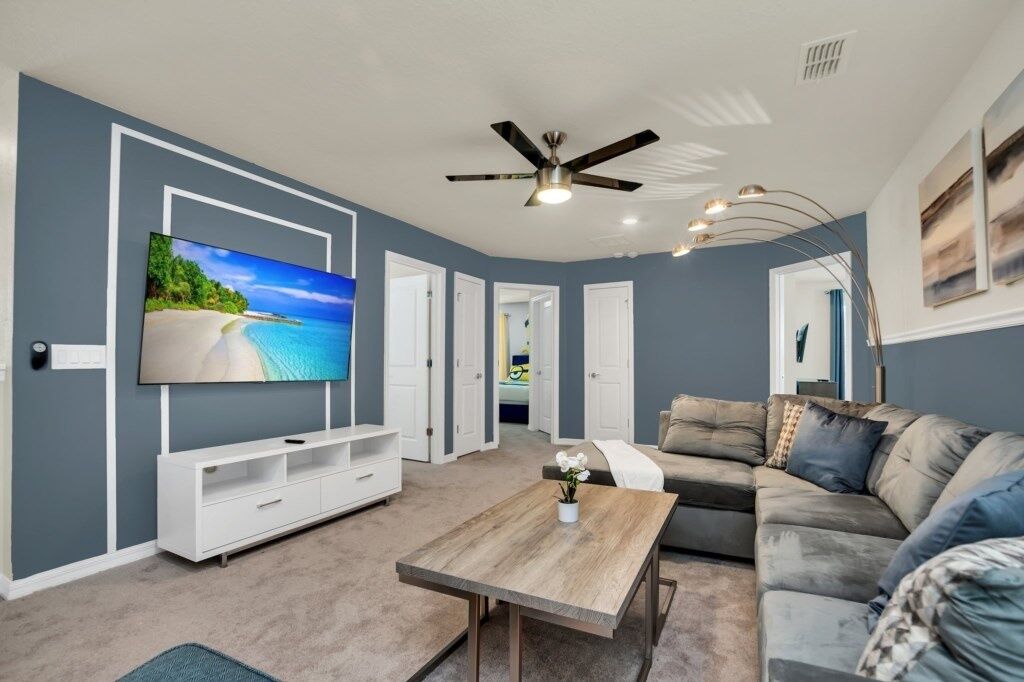 A modern living room with a flat-screen TV, a ceiling fan, a wooden coffee table, and a grey sofa.