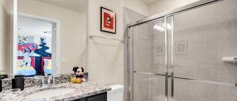 A modern bathroom with a glass shower enclosure, a marble sink, and a toilet.