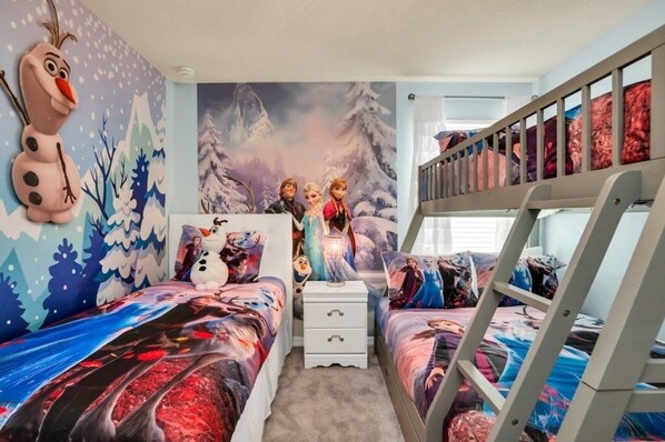 A child's bedroom with a winter theme, featuring a bunk bed, two beds with matching bedding, a dresser, and a wall mural with snowmen and a snowy landscape.