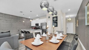Un comedor moderno con una mesa de madera dispuesta para una comida, sillas grises tapizadas y una cocina al fondo.