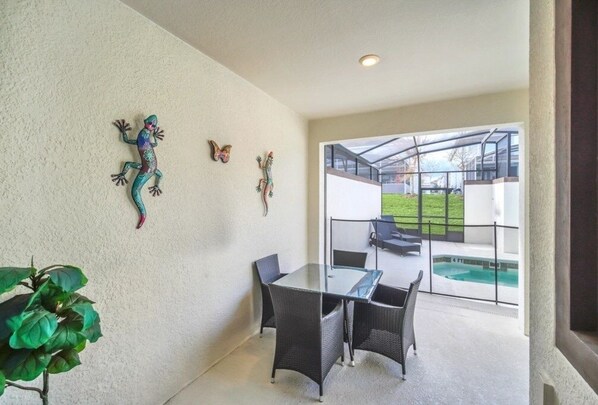 Une terrasse moderne avec une table et des chaises en verre, des éléments décoratifs muraux et une vue sur une piscine.