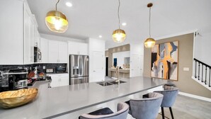 A modern kitchen with white cabinets, stainless steel appliances, a large island with bar stools, and pendant lighting. - 2900penolpe 9 Bedroom Home (Kissimmee)