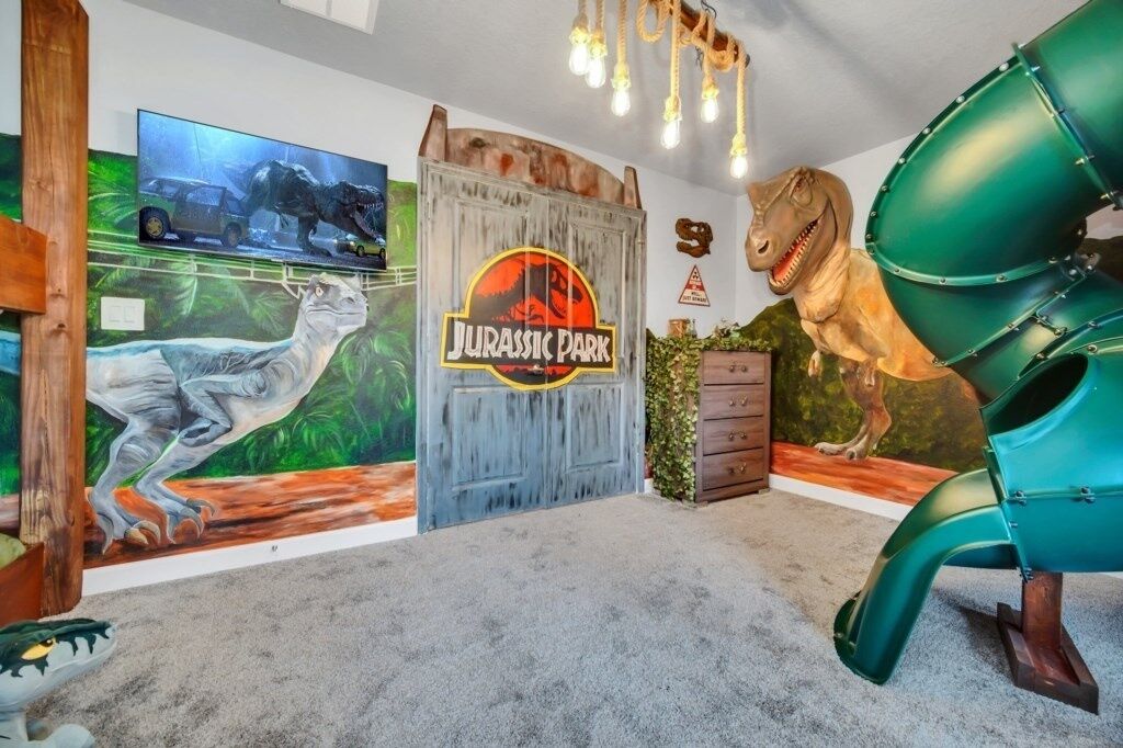 Une pièce avec un mur décoré sur le thème de « Jurassic Park », une sculpture de dinosaure et un toboggan vert.