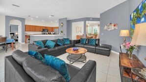 A modern living room with a black leather sofa, a wooden coffee table, and a kitchen in the background.