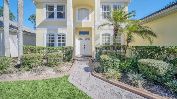 A two-story house with a central entrance, surrounded by well-maintained landscaping and palm trees.