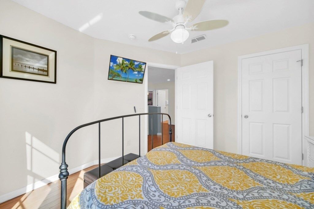 A bedroom with a bed, a ceiling fan, a door, and a framed picture on the wall.
