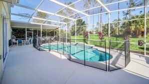 A covered outdoor swimming pool with a glass enclosure, surrounded by a grassy area and trees.