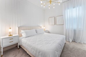 A bedroom with a large bed, white nightstands, a chandelier, and sheer curtains. - Elegant & Fun Pool/spa Games Room! 12 Bedroom Villa (Kissimmee)