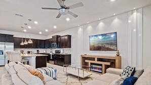 A modern living room with a sofa, a fireplace, and a kitchen in the background. - Windsor Island Resort 10 Bedroom Luxury Villa 2031 10 Villa (Davenport)