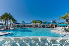 Piscina de resort com águas azul-claras, cercada por palmeiras e espreguiçadeiras.