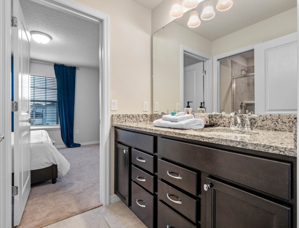 A modern bathroom with a granite countertop, dark cabinetry, and a large mirror.