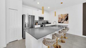 A modern kitchen with white cabinets, stainless steel appliances, and a central island with bar stools. - Luxury 4 Bedroom Storey Lake Townhome 2444Reading 4 Townhouse (Kissimmee)