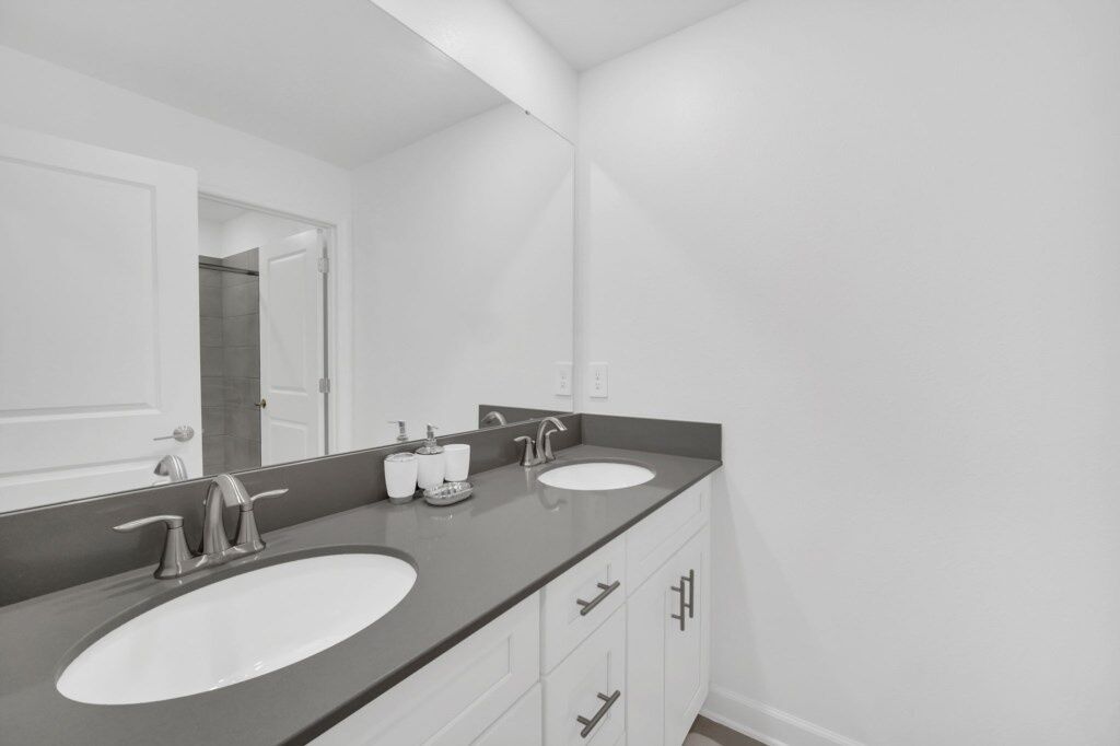 A bathroom with two sinks, a large mirror, and a door leading to another room.