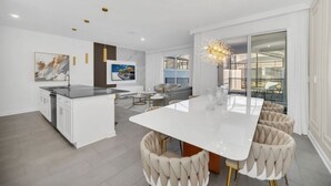 A modern kitchen with a central island, a dining area with a white table, and a seating arrangement with cushioned chairs. - Luxury 4 Bedroom Storey Lake Townhome 2444Reading 4 Townhouse (Kissimmee)
