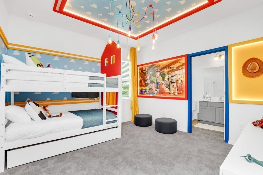Quarto de criança com beliches, um mural colorido e uma cozinha visível por uma porta aberta.