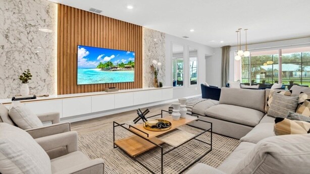 A modern living room with a large flat-screen TV, comfortable seating, and a view of the outdoors through large windows. - Dynamic 15 Bed With Character Bedrooms Pool, Spa! 15 Villa (Kissimmee)