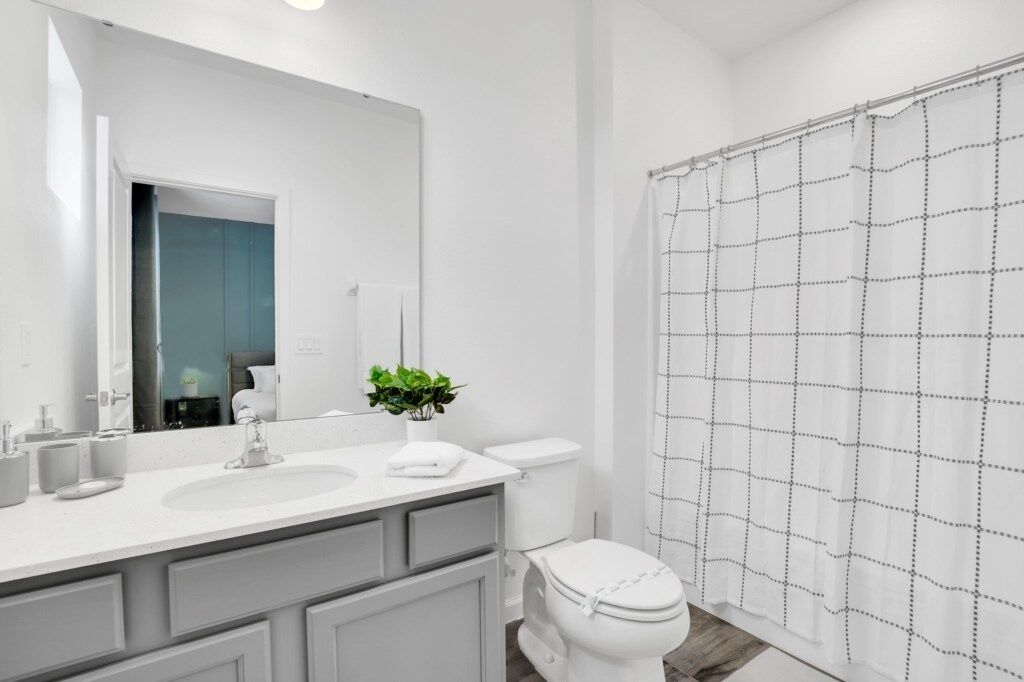 A modern bathroom with a white sink, two mirrors, a toilet, and a shower curtain with a grid pattern.