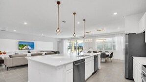 Une cuisine moderne dotée d’un îlot central, d’appareils électroménagers en acier inoxydable et de luminaires suspendus.