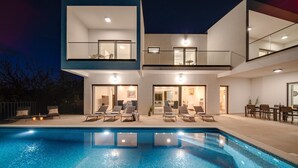 Ein modernes, zweistöckiges Haus mit Schwimmbad, Sitzgelegenheiten im Freien und Essbereich.