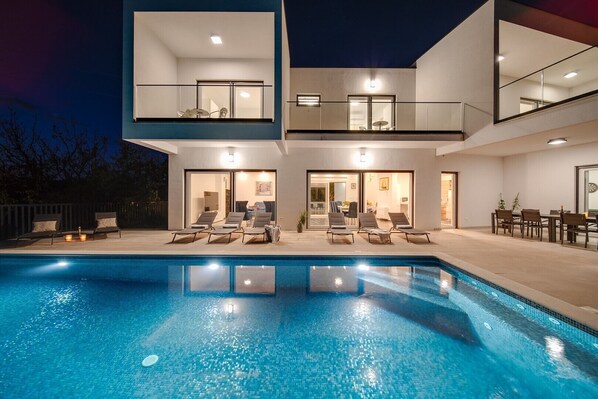 A modern two-story house with a swimming pool, outdoor seating, and a dining area.