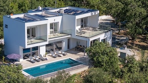 Ein modernes, zweistöckiges Haus mit einer Solaranlage auf dem Dach, einem Schwimmbecken und einer Terrassenanlage mit Liegestühlen.