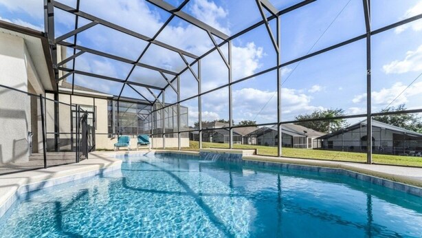 Une piscine dotée d’une structure en verre, entourée d’une armature métallique, sous un ciel dégagé.