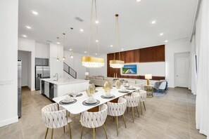 Une cuisine moderne avec des meubles blancs, un îlot central et un coin repas agrémenté d’une table blanche dressée pour six personnes.