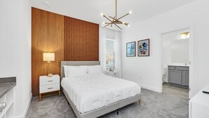 Une chambre à coucher moderne avec un mur d’accent en bois, un lit blanc, une table de chevet avec une lampe et un luminaire au plafond.