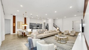 Un vaste salon comprenant un canapé, une table basse et des fauteuils, un coin repas avec une table et des chaises, et une cuisine à l’arrière-plan.
