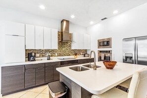 A modern kitchen with dark cabinets, a white countertop, a stainless steel sink, a microwave, and a refrigerator. - 6 Bed Pool/spa Game Room In Golf Resort! 6 Bedroom Villa (Davenport)