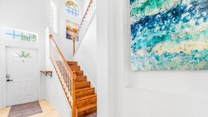 Un escalier avec des marches en bois et des murs blancs, menant à une porte dotée d’une fenêtre.