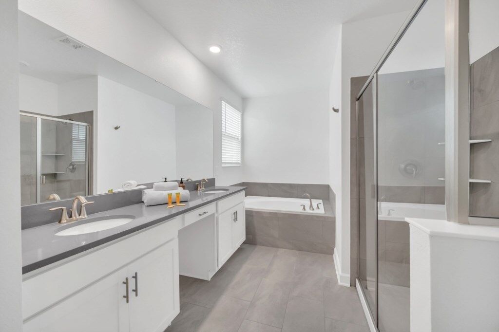 Une salle de bain moderne avec un meuble-lavabo à deux vasques, un grand miroir, une baignoire et une cabine de douche en verre.