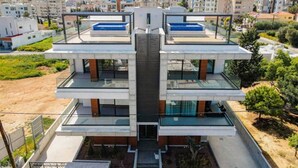 Un immeuble moderne à plusieurs étages, doté d’un atrium central, de balcons en verre et d’une piscine située au dernier étage.