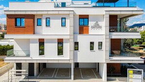 Un bâtiment moderne à plusieurs étages, doté d’un toit plat, d’un logo portant l’inscription « OXFORD HOUSE » et d’un espace de stationnement avec des places délimitées.