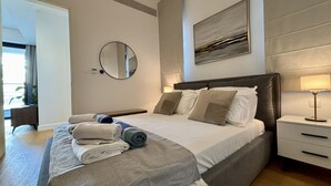 Une chambre à coucher moderne avec un grand lit, une table de chevet, une lampe, un miroir et un tableau accroché au mur.