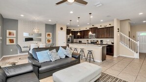 A modern living room with a black leather sofa, a white ottoman, and a dining area with a gray sofa and white cushions. - Themed Bedrooms & Private Pool Gated in Fun Resort 4 Townhouse (Kissimmee)