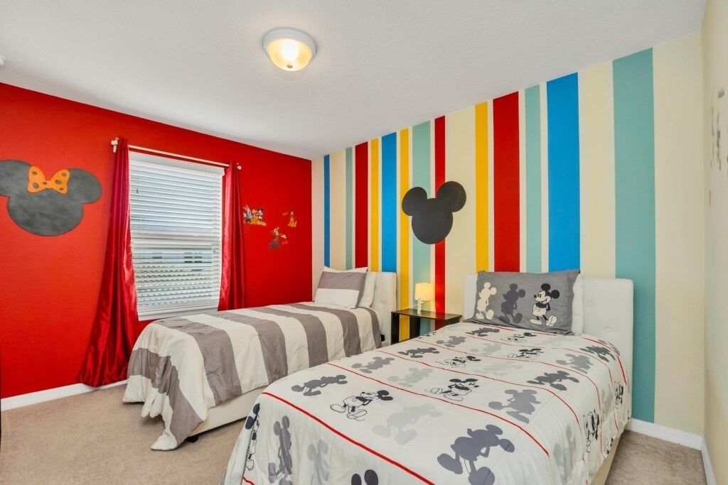 A bedroom with two beds, red walls, Mickey Mouse decorations, and a striped wall design.