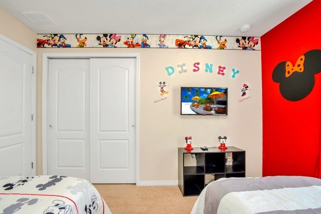Una habitación con una pared temática de Disney, un televisor y una cama con colcha de Mickey Mouse.