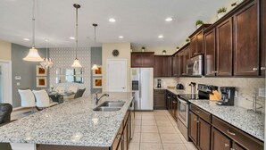A modern kitchen with granite countertops, dark wooden cabinets, stainless steel appliances, and pendant lighting. - Themed Bedrooms & Private Pool Gated in Fun Resort 4 Townhouse (Kissimmee)