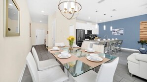 Un comedor moderno con una mesa de vidrio, sillas blancas y un candelabro central.