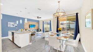 Una cocina moderna con una isla central, armarios blancos y un televisor de pantalla plana montado en la pared.
