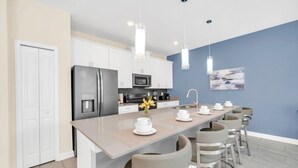 Una cocina moderna con armarios blancos, una isla central con taburetes de bar, un refrigerador y un microondas.