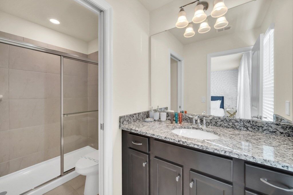 A modern bathroom with a glass shower enclosure, a white toilet, a granite countertop sink, and a large mirror.