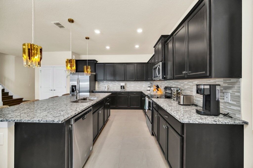 A modern kitchen with dark cabinetry, granite countertops, stainless steel appliances, and pendant lighting.
