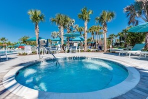 Une piscine circulaire entourée d’une terrasse bordée de palmiers, avec des chaises longues et des parasols.