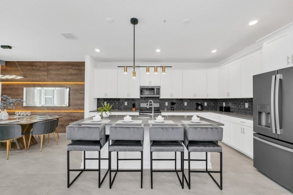 A modern kitchen with white cabinets, a central island with bar stools, a large refrigerator, and a pendant light fixture.