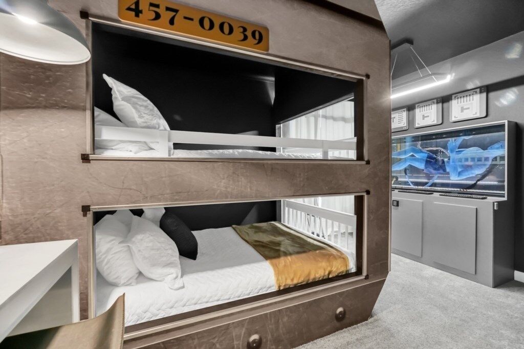 Een stapelbed met een nummerbord erboven, een bureau en een televisie op de achtergrond.